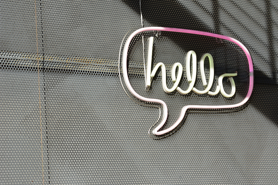 Neon sign in the shape of a speech bubble that says ‘hello’ hanging on a metal wall