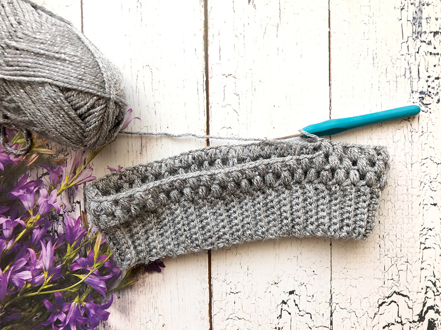 Wooden table with gray yarn, knitting needle, and knitted scarf